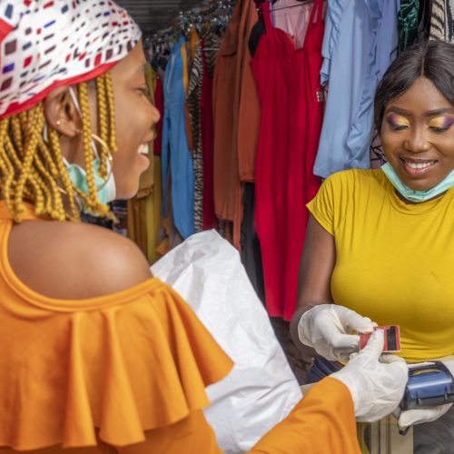 A closeup of an African female with latex gloves and a facemask paying with a credit card at a shop